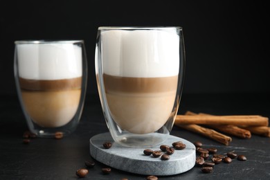 Photo of Delicious latte macchiato, cinnamon sticks and coffee beans on black table