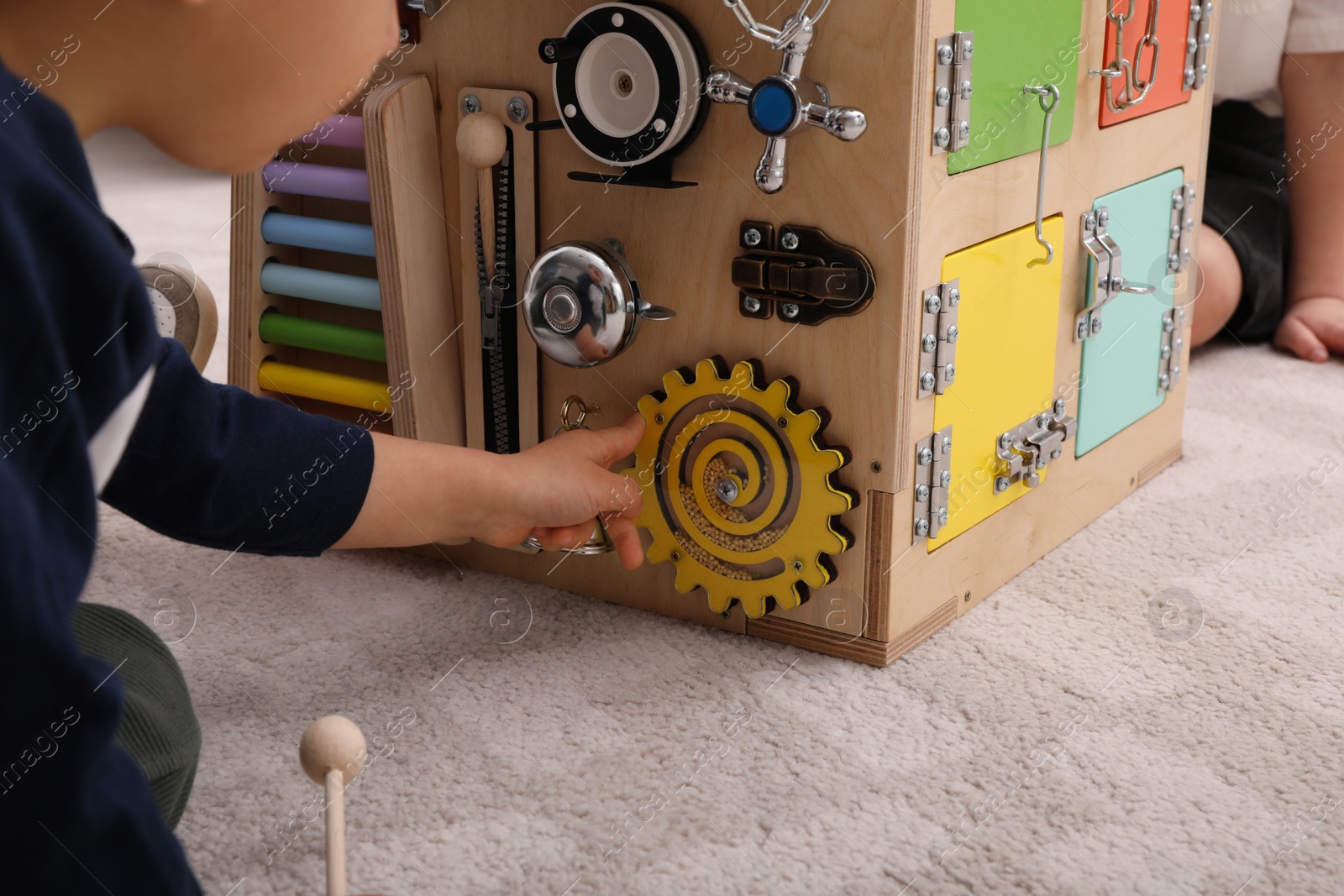 Photo of Little children playing with busy board cube on floor in room, closeup