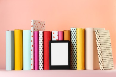 Modern e-book reader and hard cover books on pink background