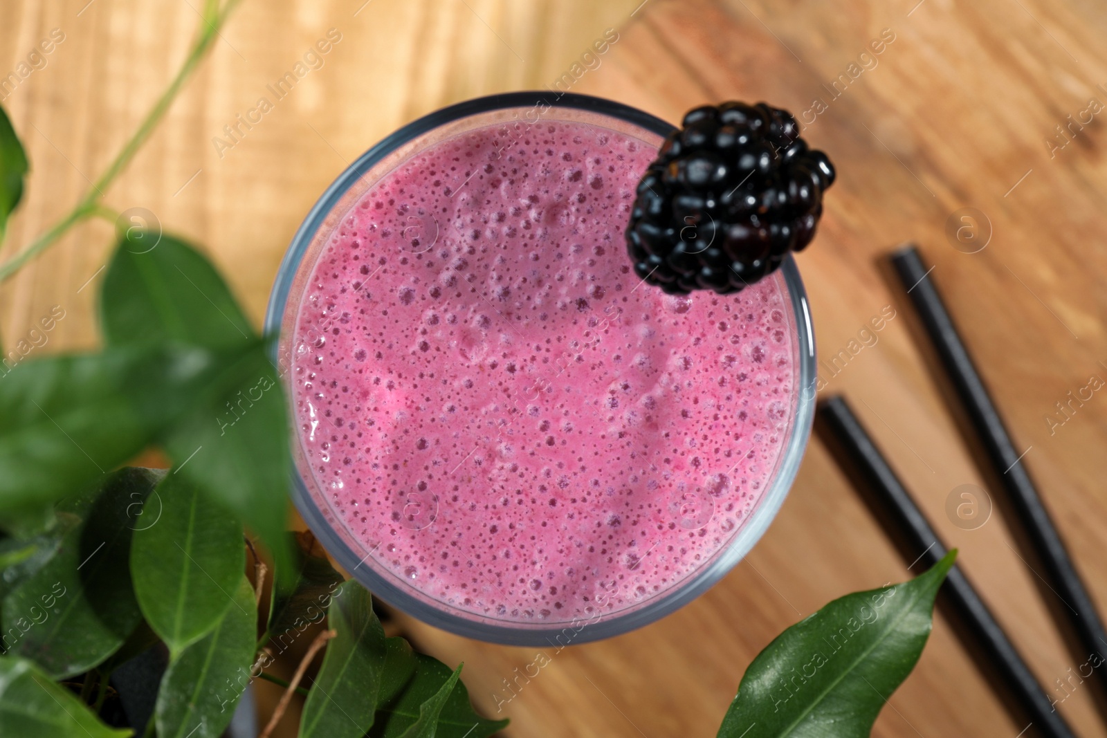 Photo of Glass of blackberry smoothie and green leaves on wooden table, flat lay