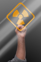 Man touching radiation warning symbol on digital screen against grey background, closeup
