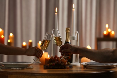 Photo of Couple clinking glasses of champagne at table with burning candles, closeup