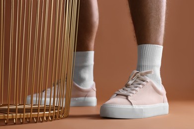 Man wearing stylish sneakers on brown background, closeup