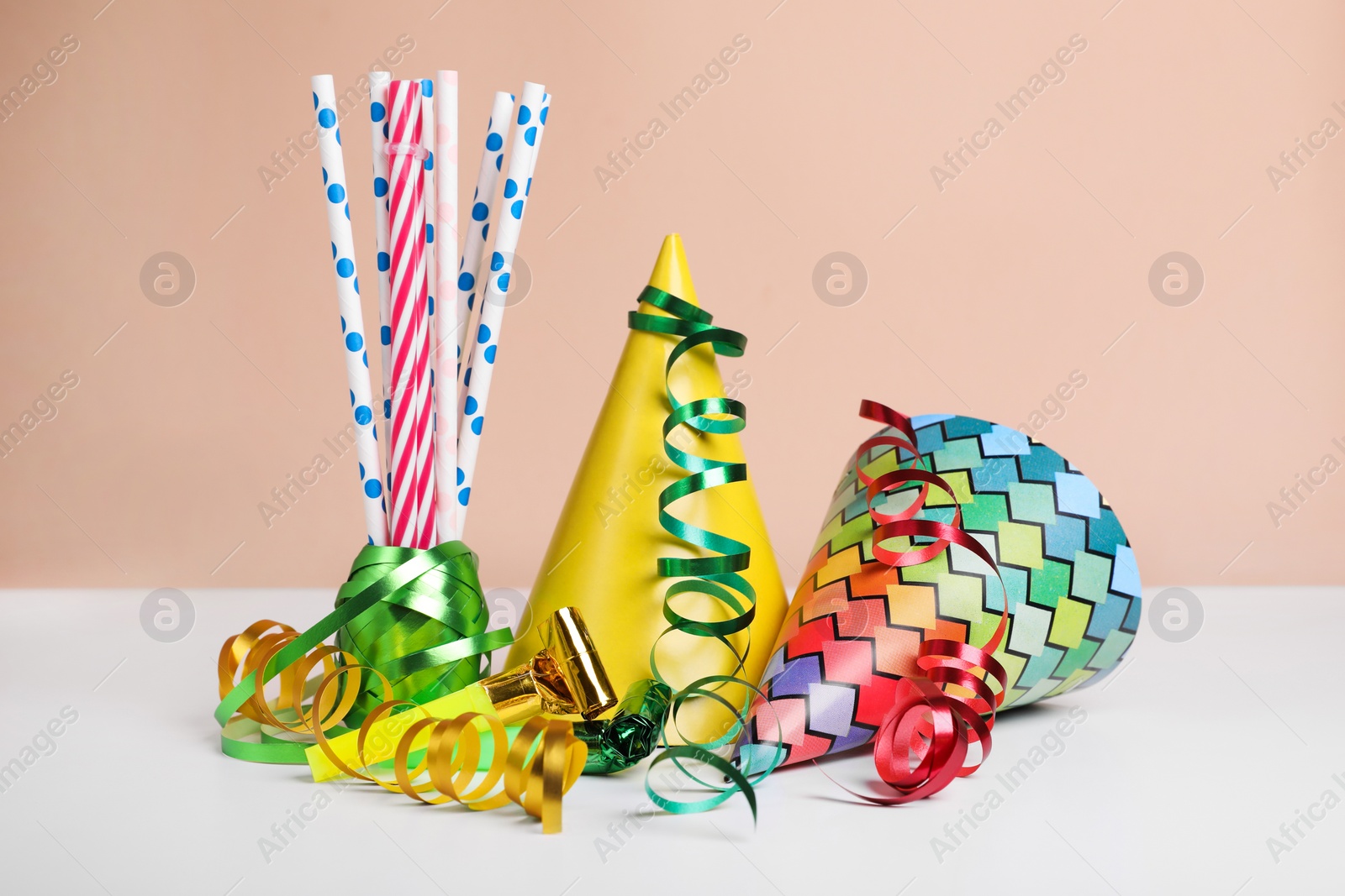 Photo of Colorful party hats, streamers and straws on white table. Birthday celebration