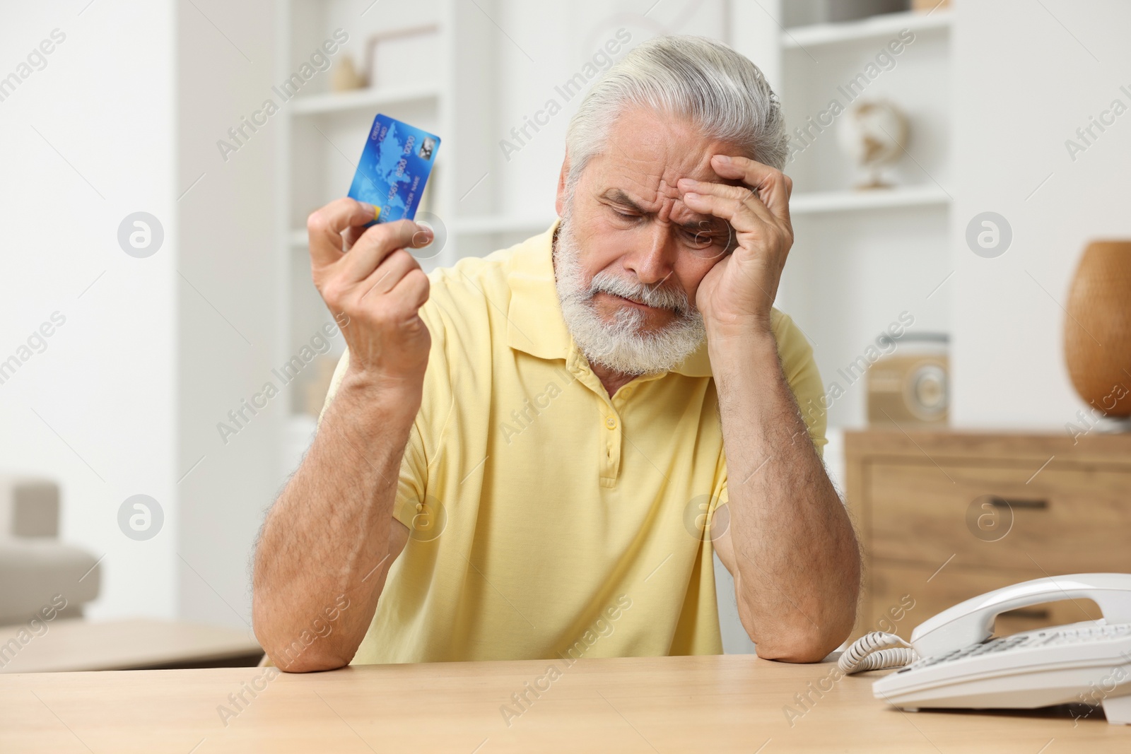 Photo of Unhappy senior man with credit card at home. Be careful - fraud