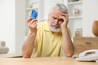 Photo of Unhappy senior man with credit card at home. Be careful - fraud