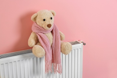 Teddy bear with knitted scarf on heating radiator near color wall
