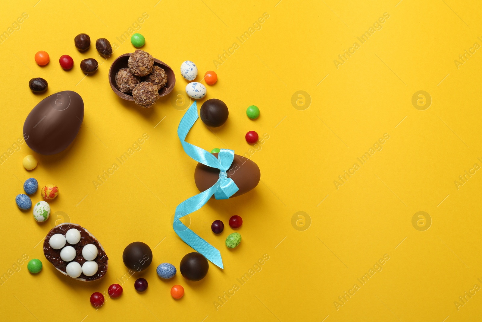 Photo of Frame of chocolate eggs and candies on yellow background, flat lay. Space for text