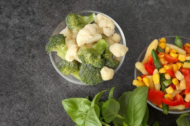 Photo of Bowls of different frozen vegetables and fresh basil on grey table, flat lay