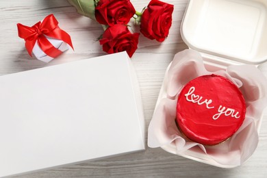 Photo of Tasty bento cake in takeaway packaging, roses and gift box on white wooden table, flat lay