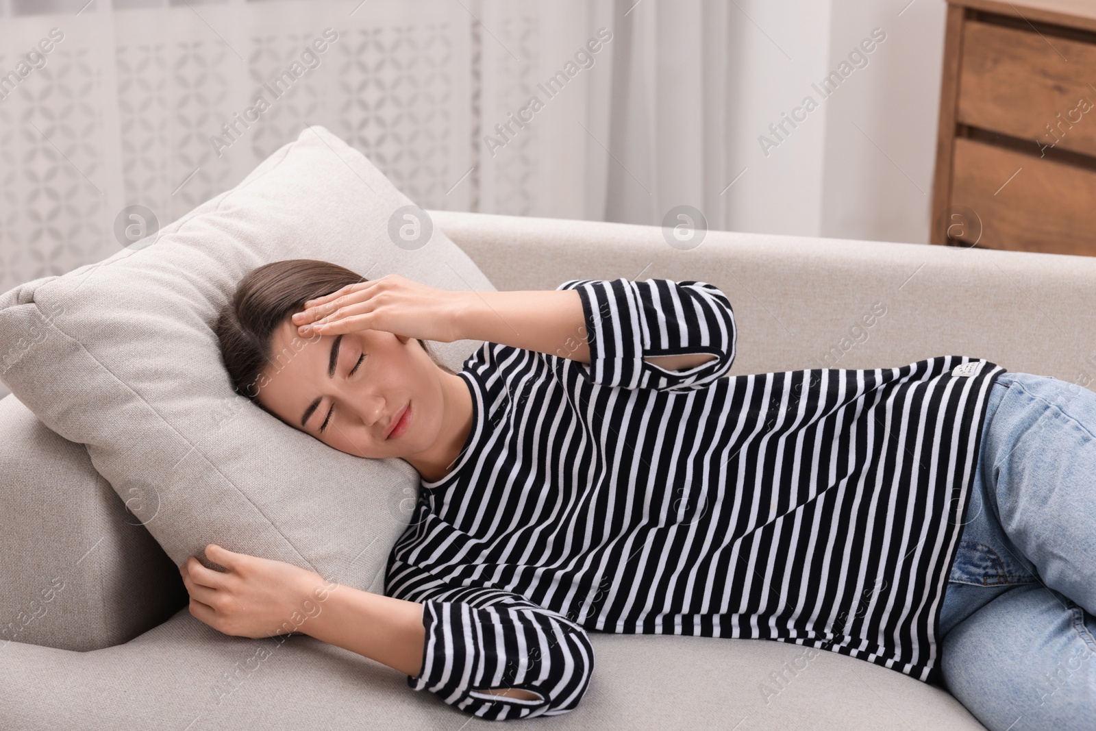 Photo of Sad woman suffering from headache on sofa indoors