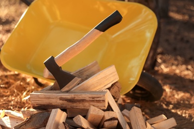 Cut firewood and axe near wheelbarrow in forest, closeup