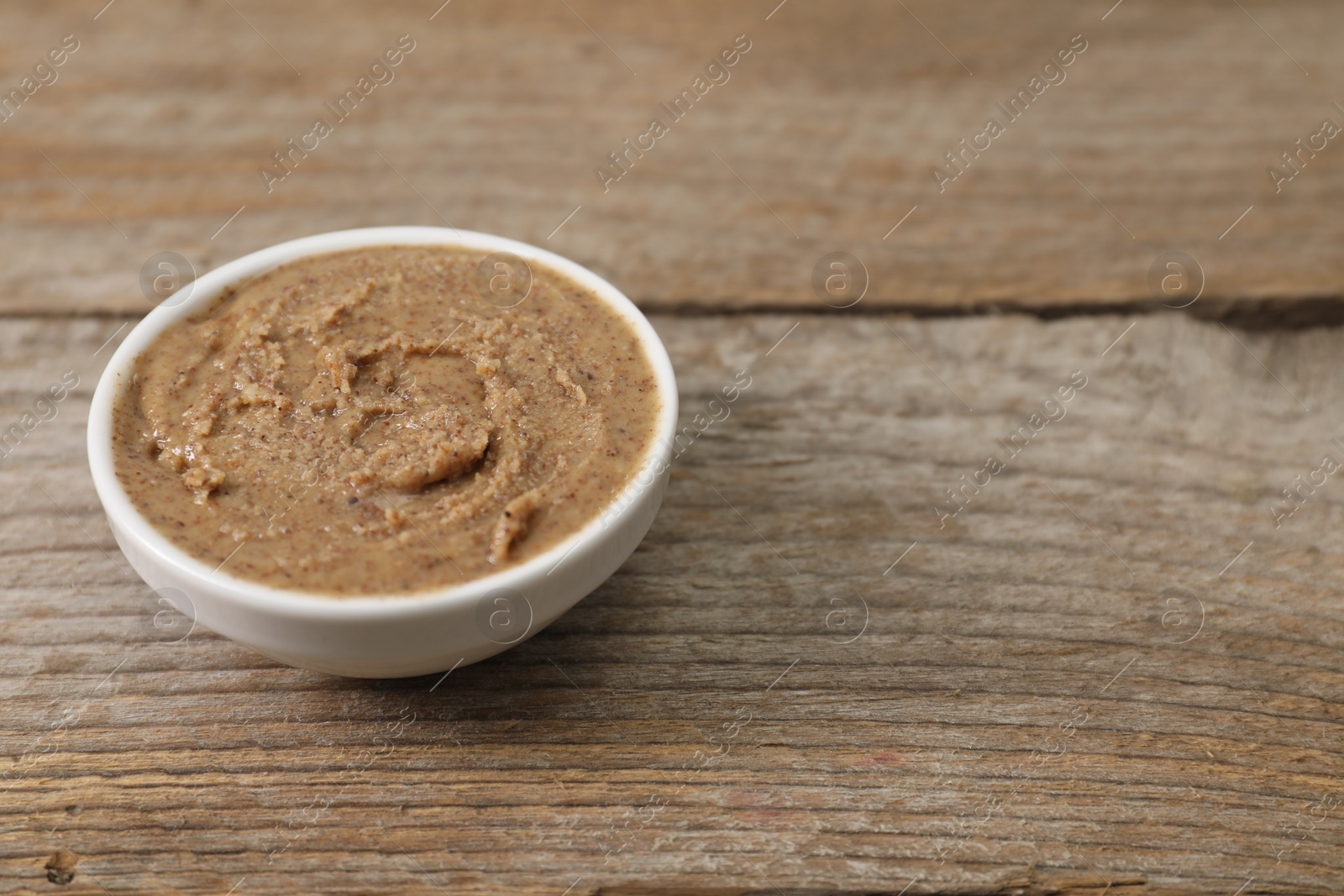 Photo of Delicious nut butter in bowl on wooden table, closeup. Space for text