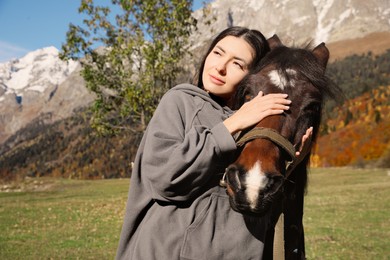 Photo of Young woman hugging horse in mountains on sunny day. Beautiful pet