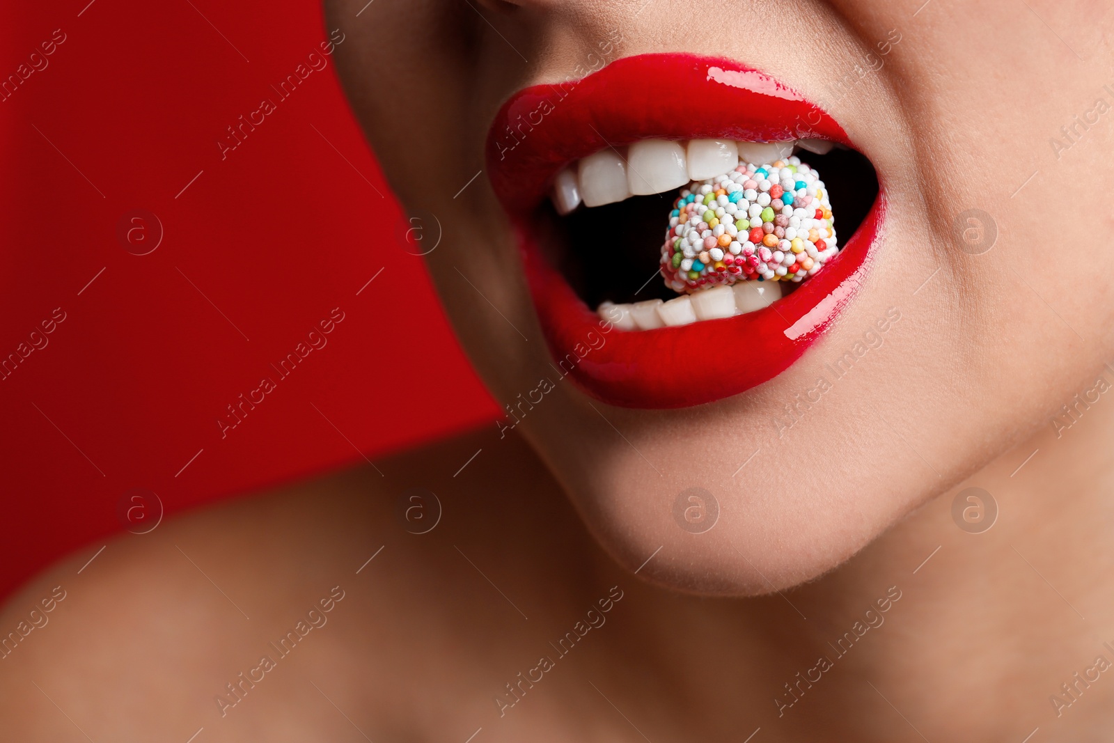 Photo of Closeup view of woman with beautiful lips eating candy on red background. Space for text