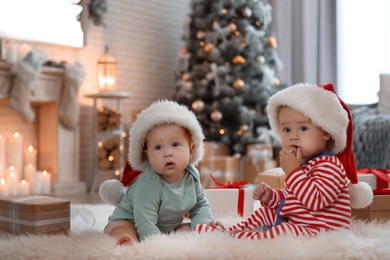 Image of Cute children in Santa hats on floor in room with Christmas tree