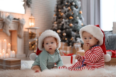 Cute children in Santa hats on floor in room with Christmas tree