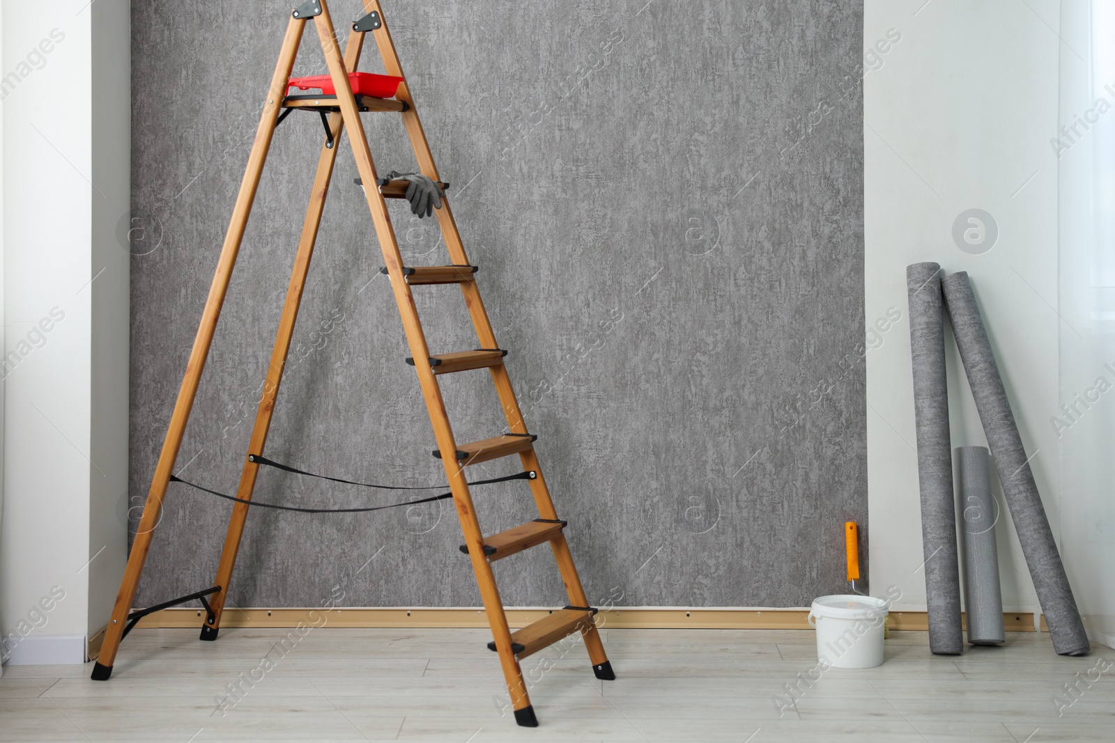 Photo of Wallpaper rolls, bucket with glue and wooden ladder in room