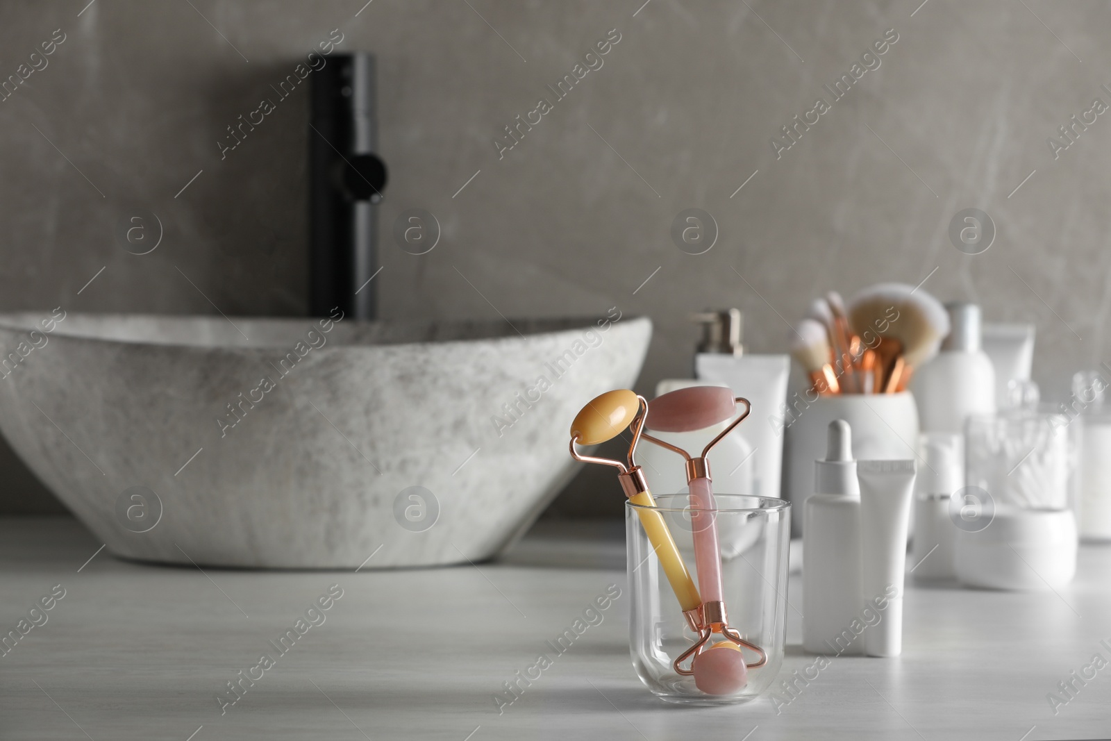 Photo of Natural face rollers and cosmetic products on counter in bathroom. Space for text