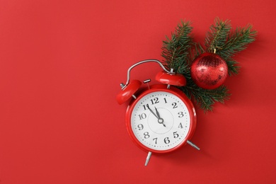Photo of Alarm clock and fir branch with Christmas ball on red background, flat lay with space for text. New Year countdown