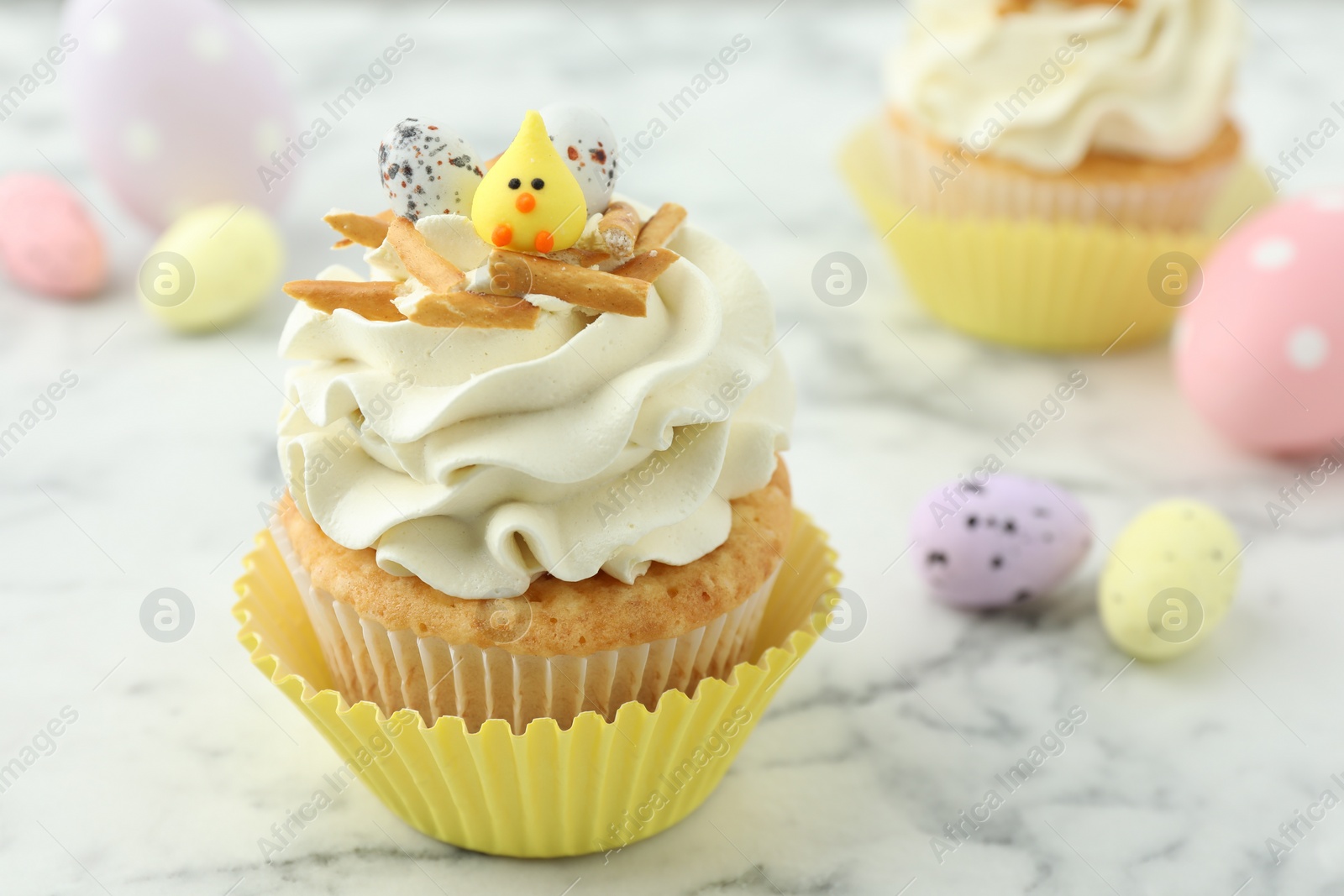 Photo of Tasty Easter cupcake with vanilla cream and candies on white marble table