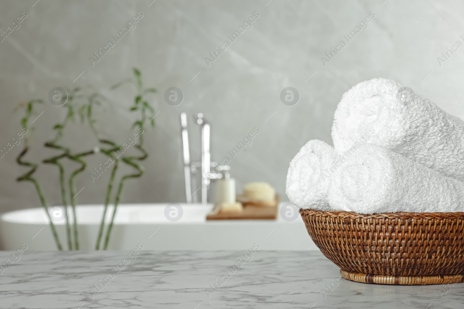 Photo of Rolled bath towels in wicker bowl indoors, space for text