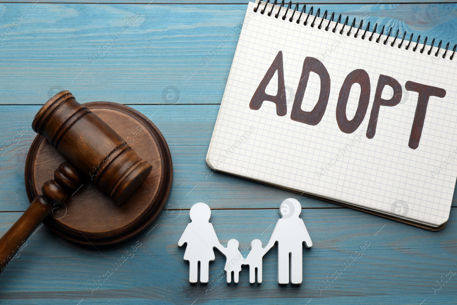 Photo of Family figure, gavel and notebook with word Adopt on light blue wooden table, flat lay