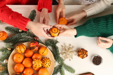 Photo of Friends decorating fresh tangerines with cloves at light table, top view. Making Christmas pomander balls