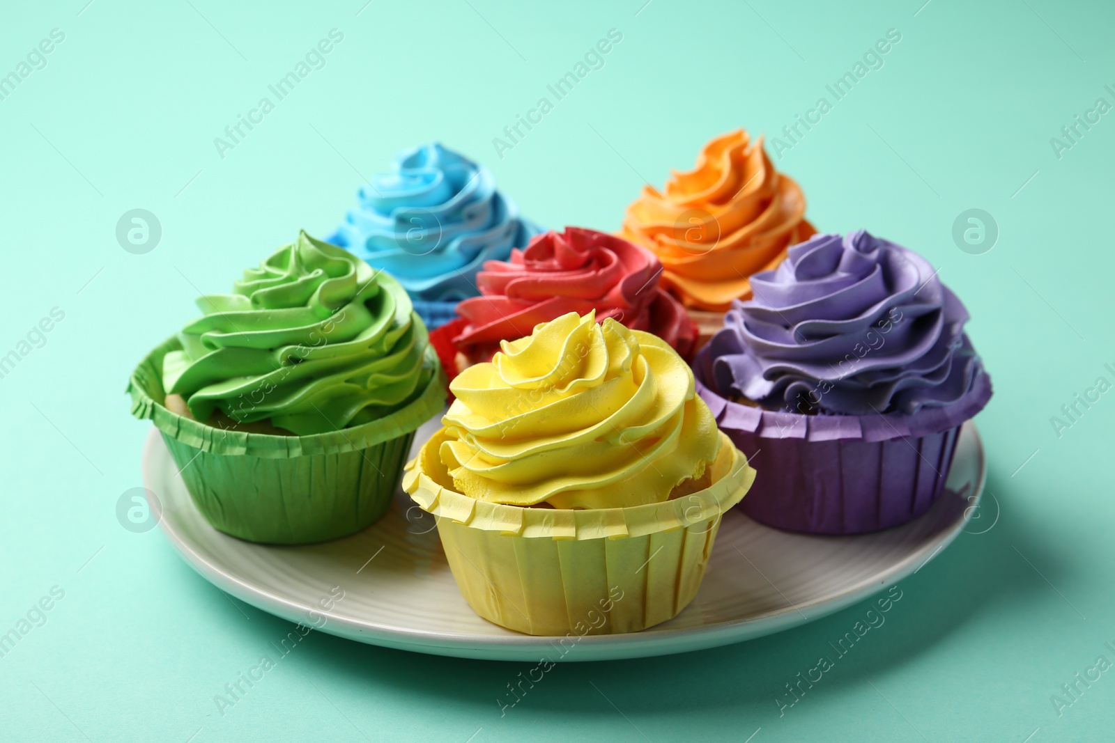 Photo of Plate with delicious bright cupcakes on turquoise background, closeup