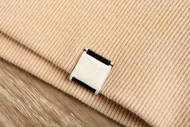 Photo of Beige apparel with blank clothing label on wooden table, top view