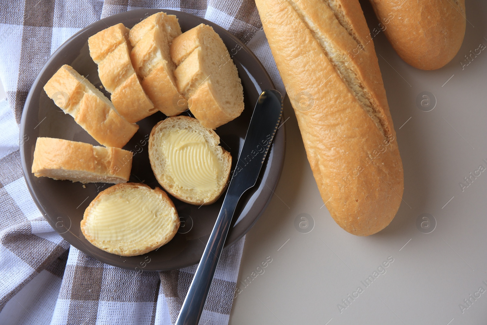 Photo of Whole and cut baguettes with fresh butter on table, flat lay