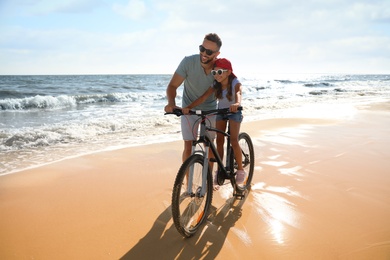 Photo of Happy father teaching daughter to ride bicycle on sandy beach near sea