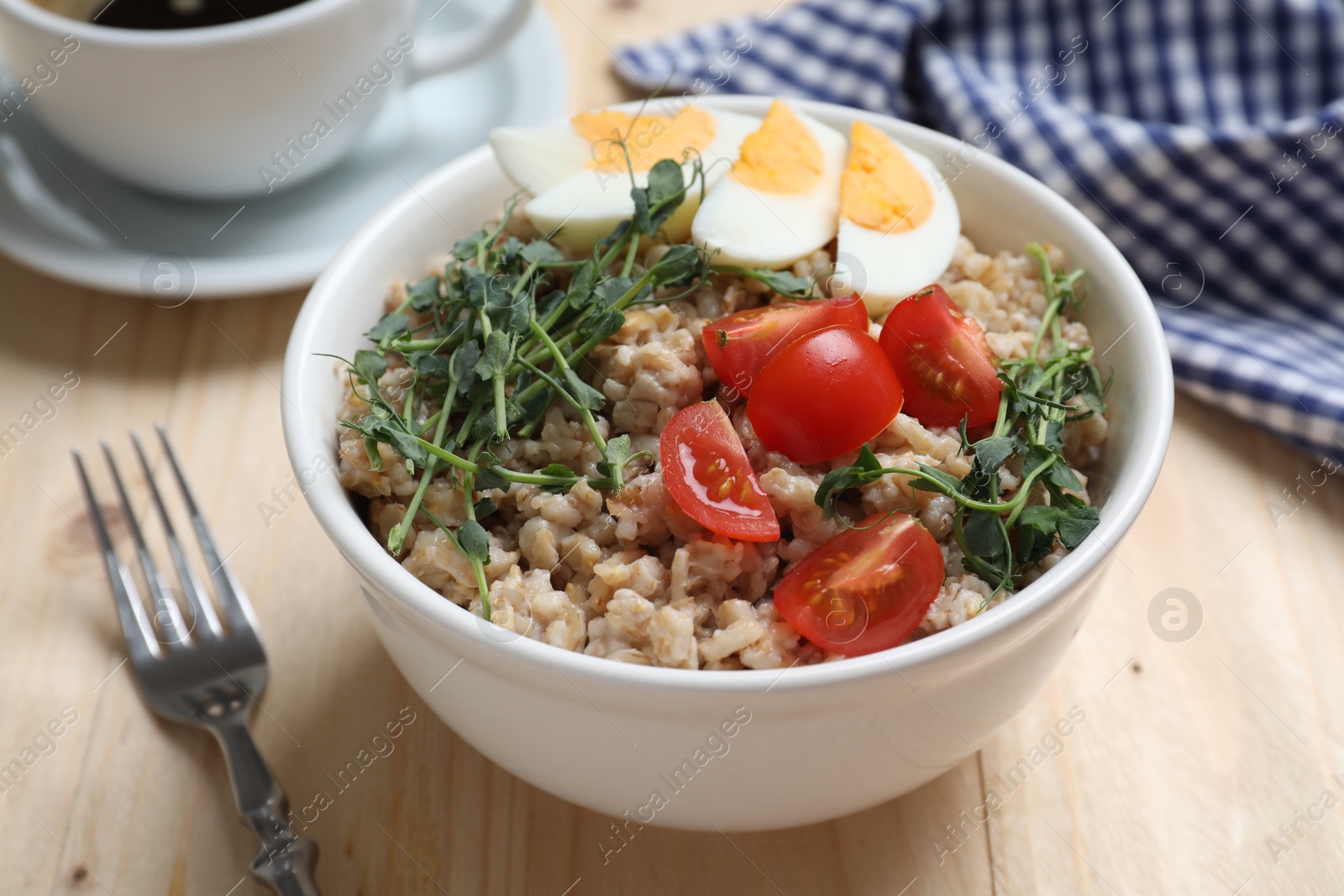 Photo of Tasty boiled oatmeal with egg and tomatoes served on wooden table, closeup