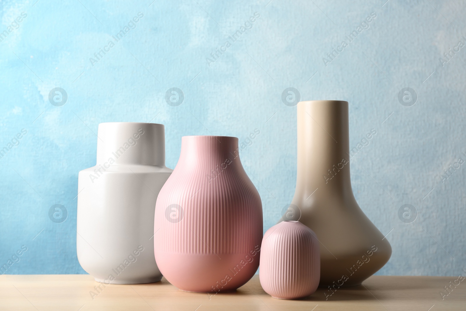 Photo of Stylish ceramic vases on wooden table against light blue background