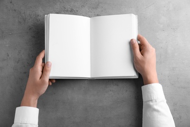 Photo of Man holding blank book at grey table, top view. Mock up for design