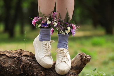 Photo of Woman standing on log with flowers in socks outdoors, closeup
