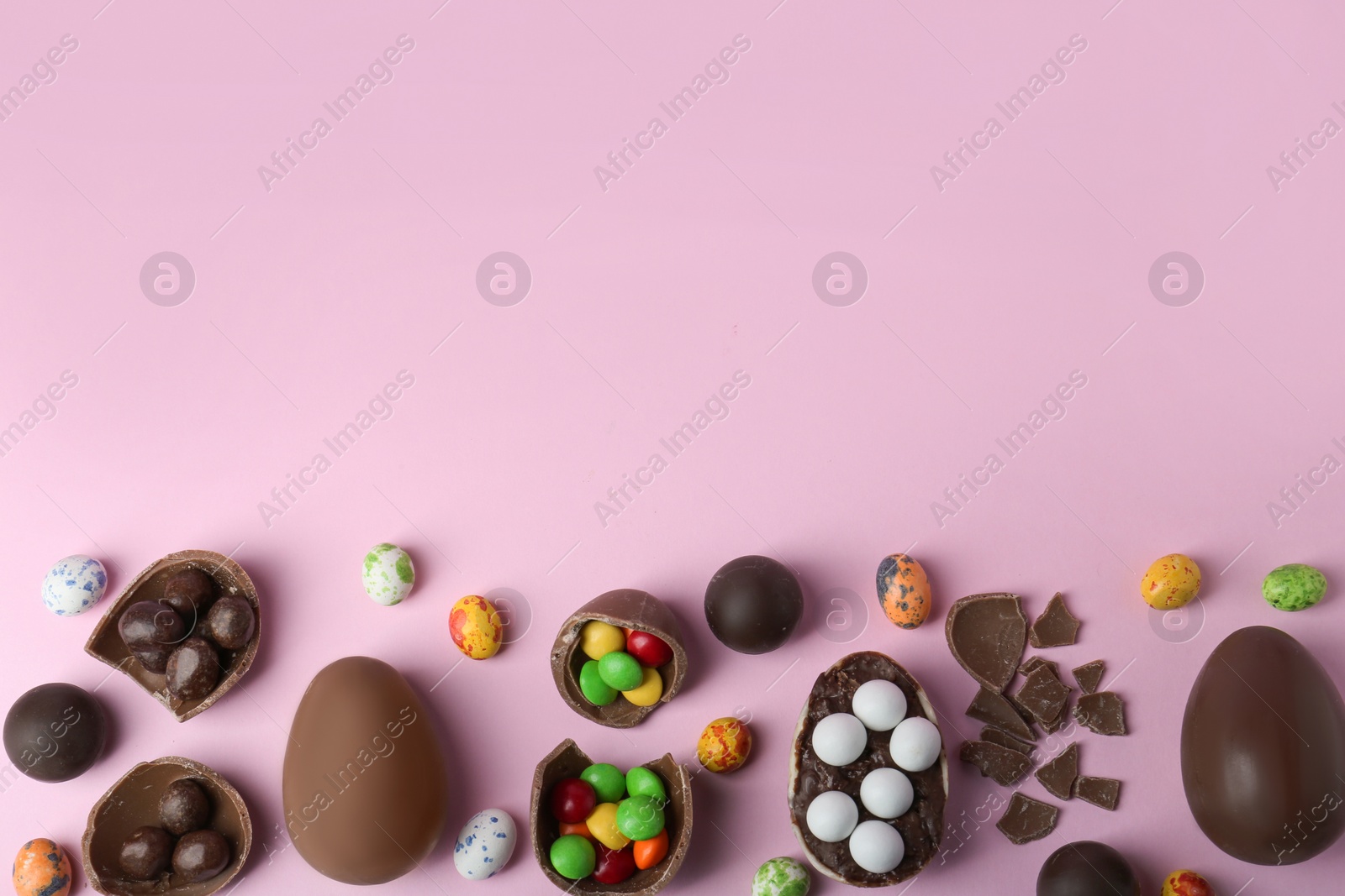 Photo of Tasty chocolate eggs and candies on pink background, flat lay. Space for text