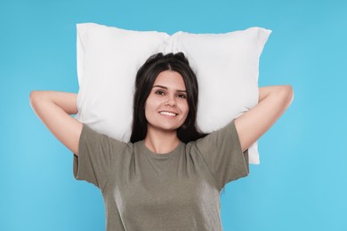 Happy young woman with soft pillow on light blue background
