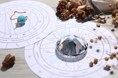 Photo of Astrology prediction. Zodiac wheels, pendulum, gemstone and dry flowers on wooden table, closeup