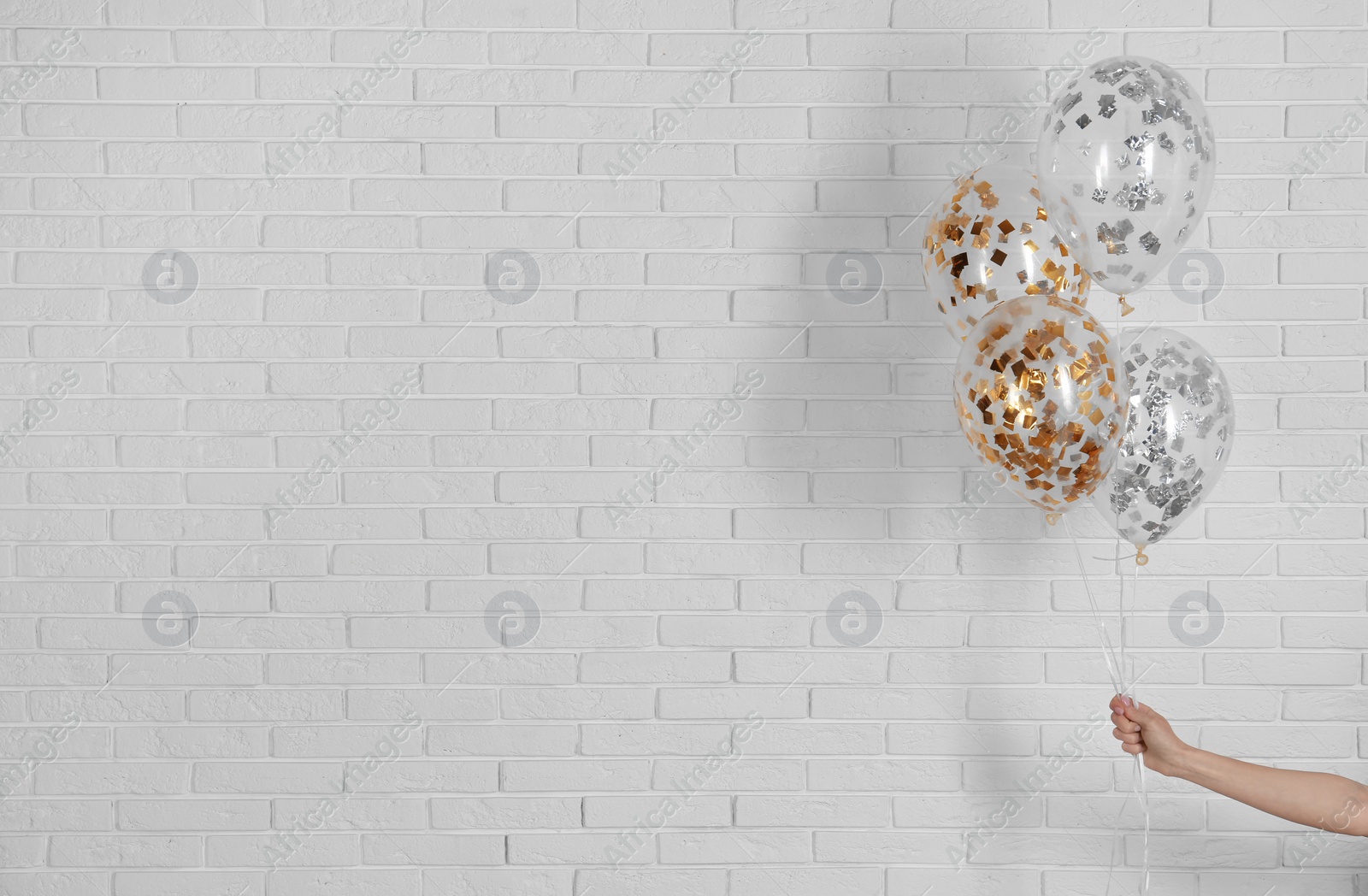 Photo of Young woman holding bright balloons near brick wall, space for text