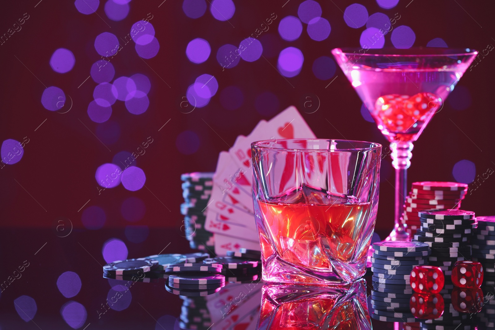 Photo of Alcohol drinks, dice, playing cards and casino chips on table against blurred lights, space for text. Straight poker combination