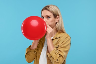 Woman blowing up balloon on light blue background
