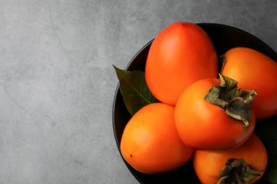 Photo of Delicious ripe persimmons in bowl on light gray textured table, top view. Space for text
