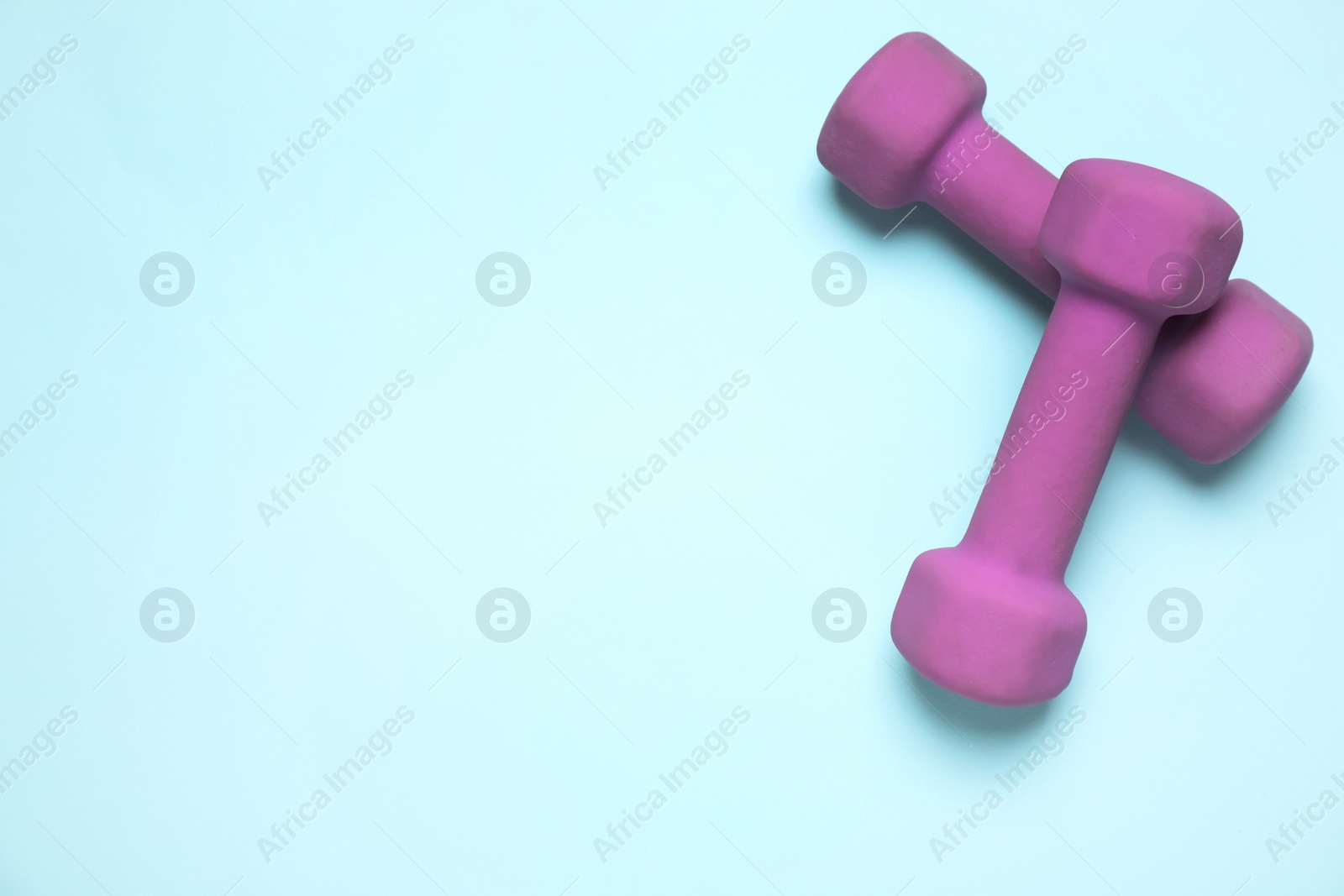 Photo of Bright dumbbells on light blue background, flat lay. Space for text