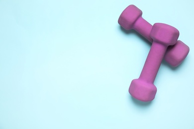 Bright dumbbells on light blue background, flat lay. Space for text