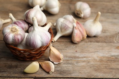 Photo of Fresh organic garlic in wicker basket on wooden table. Space for text