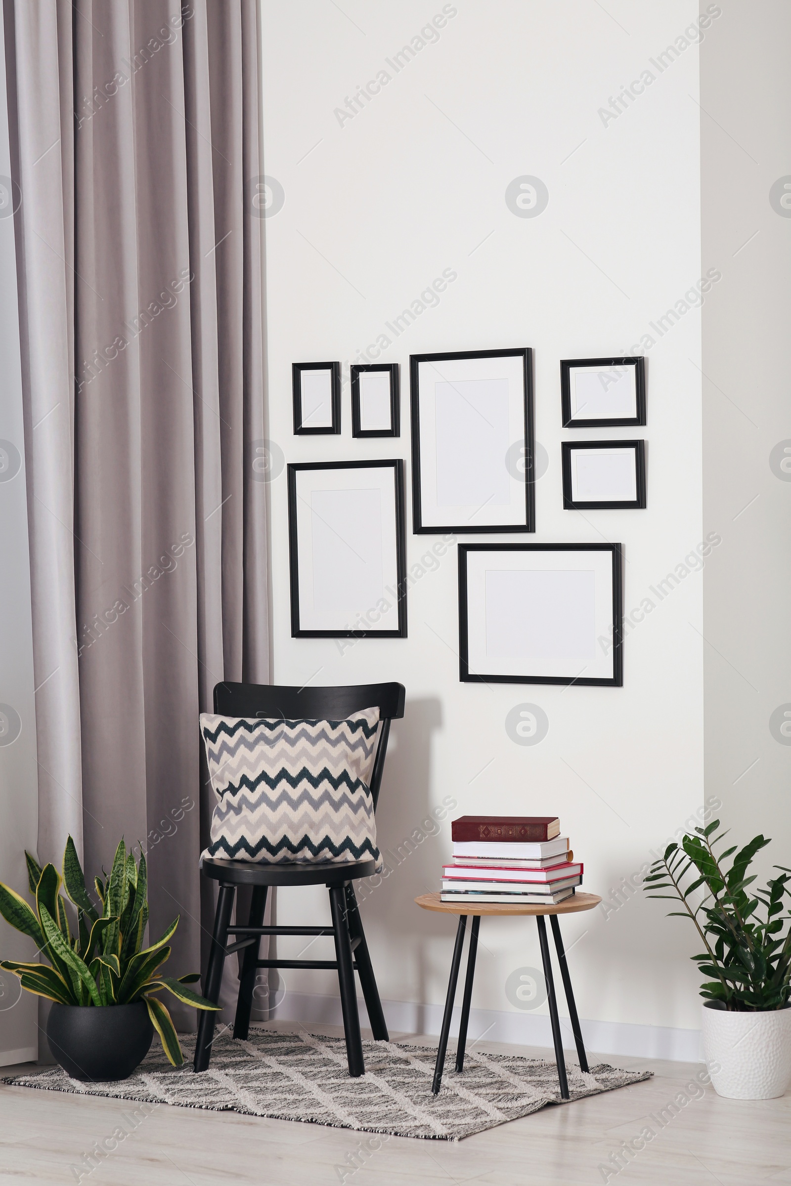 Photo of Empty frames hanging on white wall, wooden chair and table with books indoors