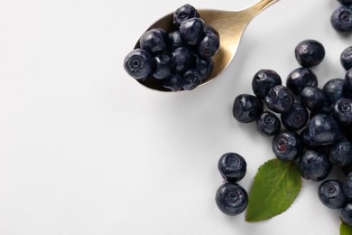 Spoon with ripe bilberries and leaf on white background, flat lay. Space for text