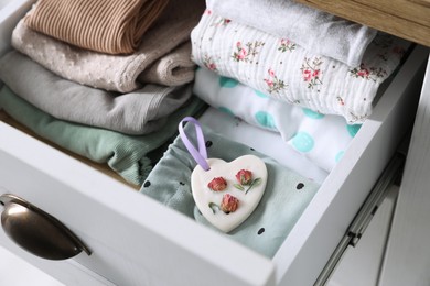 Photo of Beautiful heart shaped scented wax sachet and clothes in dresser drawer, closeup