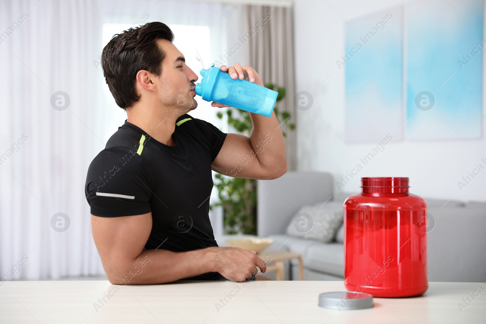 Photo of Young athletic man drinking protein shake at home